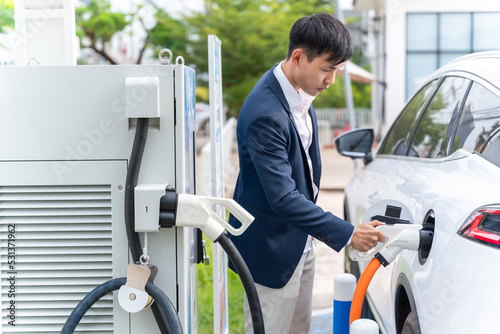 Asian man holding Electric Car Charging connect to Electric car on electric car charging station. Concept of green energy and reduce CO2 emission. EV car.