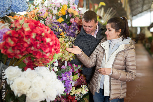 Portrait of young man and woman choosing together bouquet at flowers shop