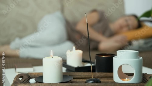 Close up of scented candles and aroma lamp. In the background woman is lying on sofa and sleeping, relaxing. Anti stress and holistic rest. Mental health concept.