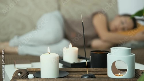 Close up of scented candles and aroma lamp. In the background woman is lying on sofa and sleeping, relaxing. Anti stress and holistic rest. Mental health concept.