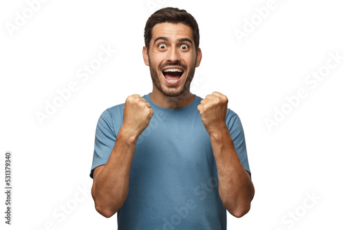 Young man isolated on gray background, celebrating victory and acting as if he is winner, squeezing fists