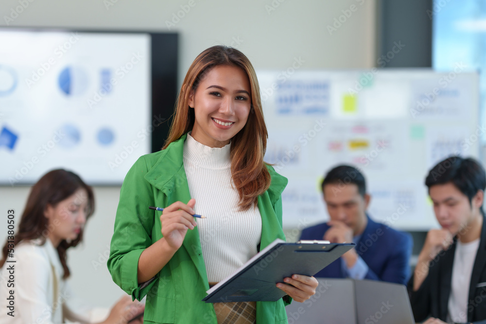 Attractive Asian businesswoman with smile standing with clipboard holding paperwork and taking note of work detail at office and looking at camera. Attractive Asian businesswoman with smile standing with clipboard holding paperwork and taking note of work detail at office and looking at camera.