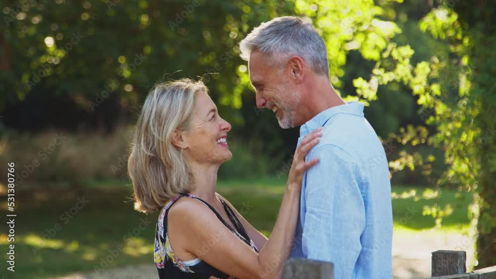 Loving casually dressed smiling mature couple meeting by wooden fence on walk in summer countryside - shot in slow motion Loving casually dressed smiling mature couple meeting by wooden fence on walk in summer countryside - shot in slow motion