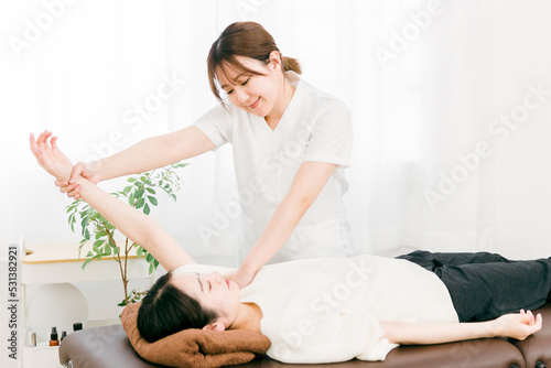 患者の腕・肩をマッサージする整体師の女性（理学療法士・作業療法士） 