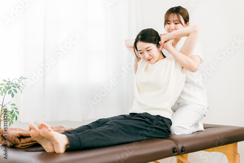 患者の肩甲骨・肩をマッサージする整体師の女性 