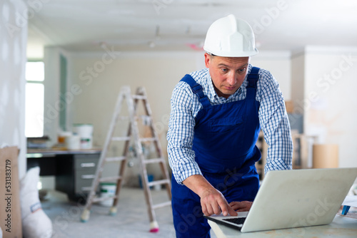 Serious builder handyman checking plan of house renovation on laptop
