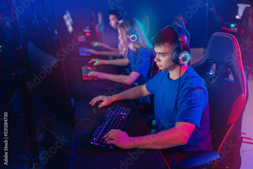 Portrait young man pro gamer with headphones playing in online video game in net cafe, neon color light, soft focus. Cybersport team concept
