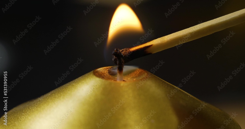 On a black background, a match lights the wick of a golden candle