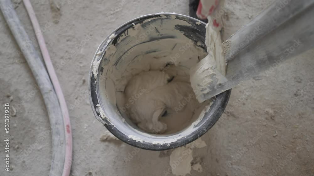 The worker rakes the excess solution into a bucket. scraping Hands of a plasterer working with plastic mastic in a white bucket. The process of applying the mortar to the wall. The worker rakes the excess solution into a bucket. scraping Hands of a plasterer working with plastic mastic in a white bucket. The process of applying the mortar to the wall.
