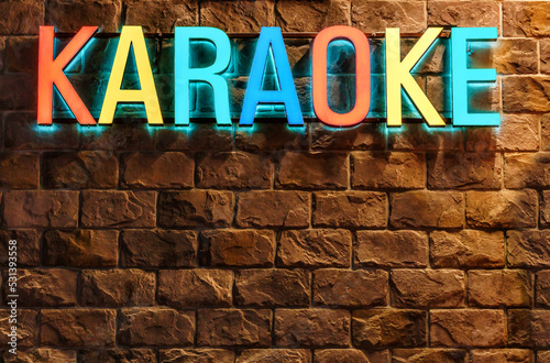 Colorful neon illuminated Karaoke sign on stone building wall background. Architectural decor of entertainment facilities. Singing karaoke concept.