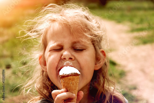 Little funny girl eats ice cream. Copy space. Cute cheerful child outdoors.