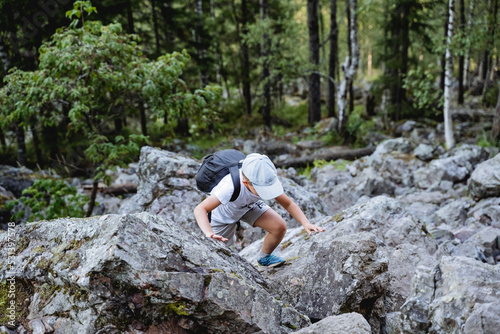 The child spends the holidays actively in a hike, children's recreation in nature, the boy walks on the stones, a little tourist with a backpack, a cap on his head, a kurumnik under his feet.