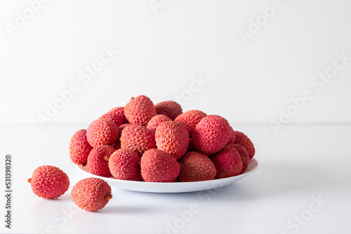 Fresh ripe lychee fruits in plate on grey wooden table. Fresh ripe litchi on white background photo