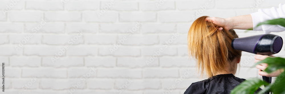 Fototapeta premium Beautiful young woman at the hairdresser blow drying her hair. Hair dryer in salon. hairstyle for a young girl. banner, wide shot