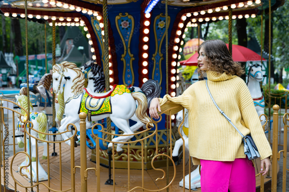 Portrait of a young happy woman on the background of a carousel in an amusement park