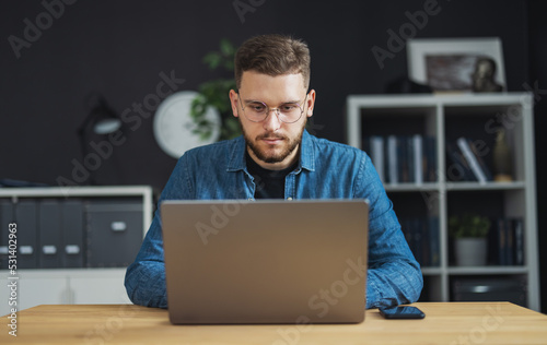 Portrait of young focused man coding on laptop, IT programmer working on creating innovative software, app, program. photo