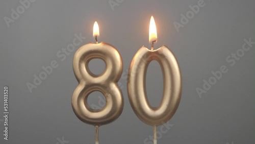 Burning gold birthday candles on gray background, number 80 photo
