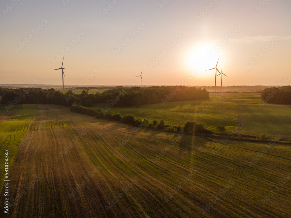 Obraz premium Green energy concept. Aerial cinematic drone panoramic shot of windmills and electricity wind turbines farm during summer sunset. Panoramic European nature view. Image contain noise and blur