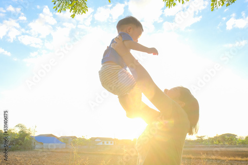 hold and lift toddler asian boy in outdoor park sunset