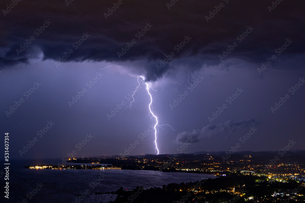 Massive lightning strike during thunderstorm over the Bodensee lake in Austria/Germany with the village Lindau in the foreground