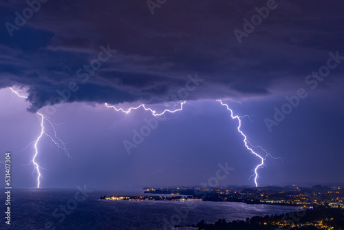 Massive double lightning strike during thunderstorm over the Bodensee lake in Austria/Germany with the village Lindau in the foreground