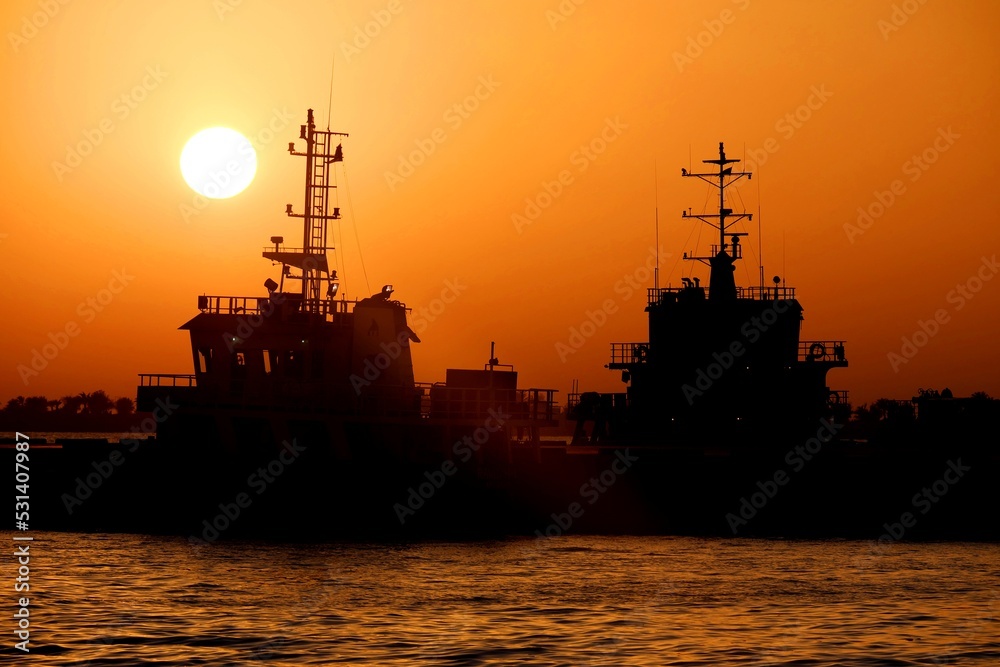 Sunset and shadows. Boat silhouette floating in the orange horizon. Sunset and shadows. Boat silhouette floating in the orange horizon.