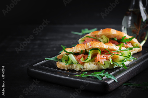 Croissants with salted salmon, cucumber and arugula served on dark background. Close up.