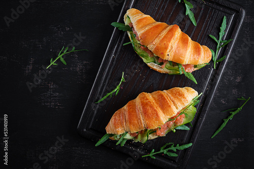 Croissants with salted salmon, cucumber and arugula served on dark background. Close up. Top view