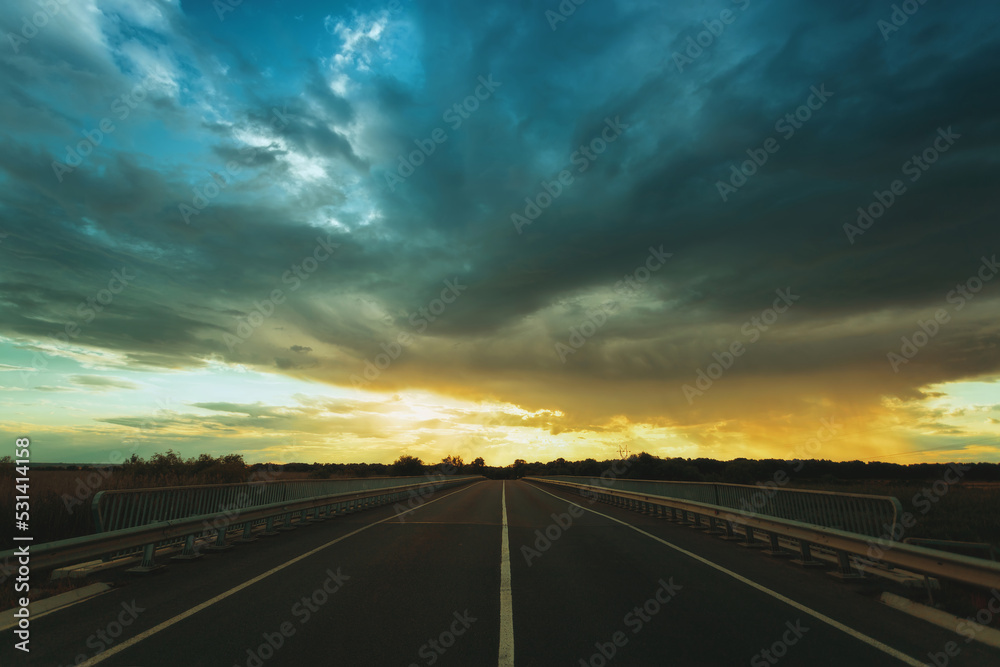 Empty highway at sunset, clouds, rays of the sun