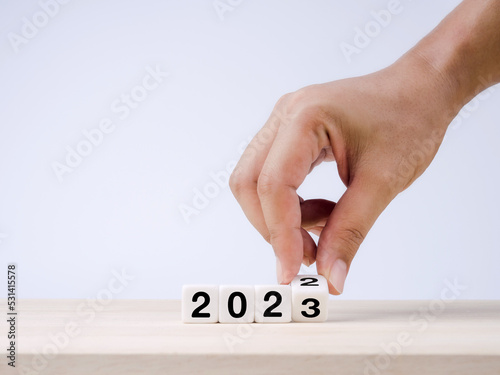 The calendar year 2022 changed to 2023, success concept. White cube blocks turning by hand for the transition from 2022 to 2023, preparation for merry Christmas and happy new year on blue background.