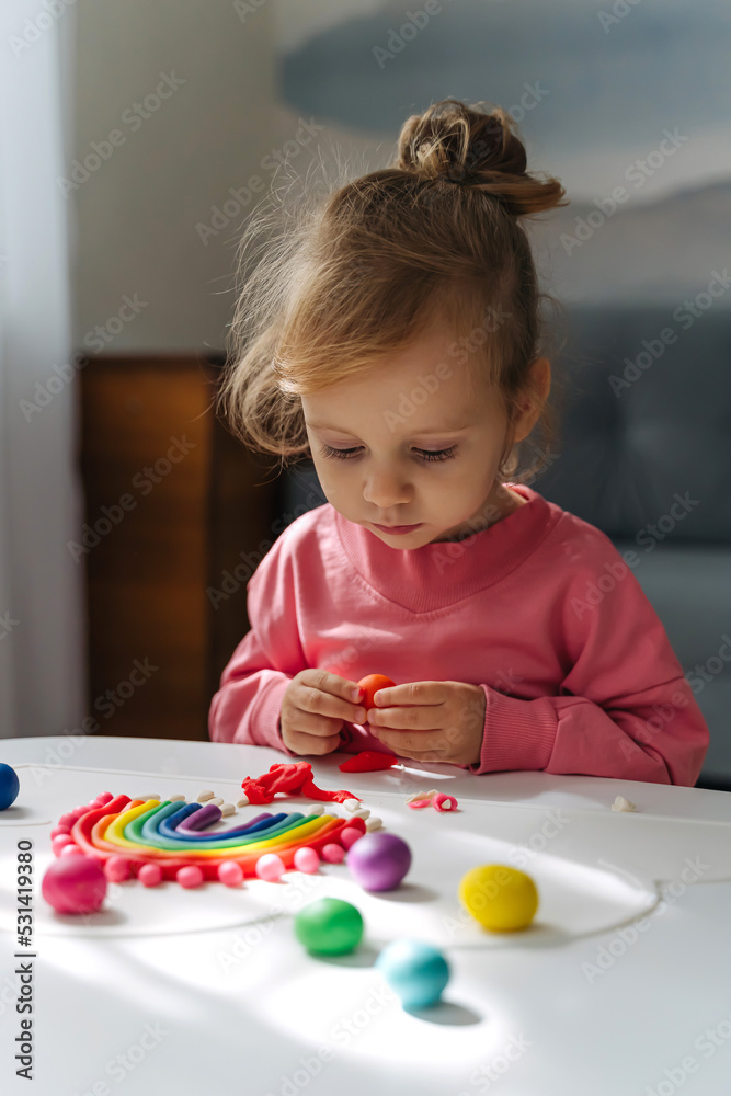 A little girl playing with rainbow from play dough for modeling. Art Activity for Kids. Fine