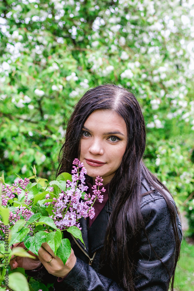 Portrait of young beautiful woman with purple lilac flowers in rainy weather on background of spring blooming garden. Portrait of young beautiful woman with purple lilac flowers in rainy weather on background of spring blooming garden.