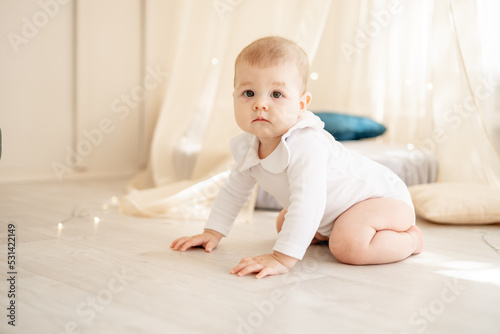 cute little baby boy or girl in a bright children's room with a wigwam in a white cotton bodysuit crawling