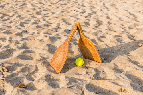 Two wooden rackets and tennis balls in a golden sandy beach on a beautiful summer day.