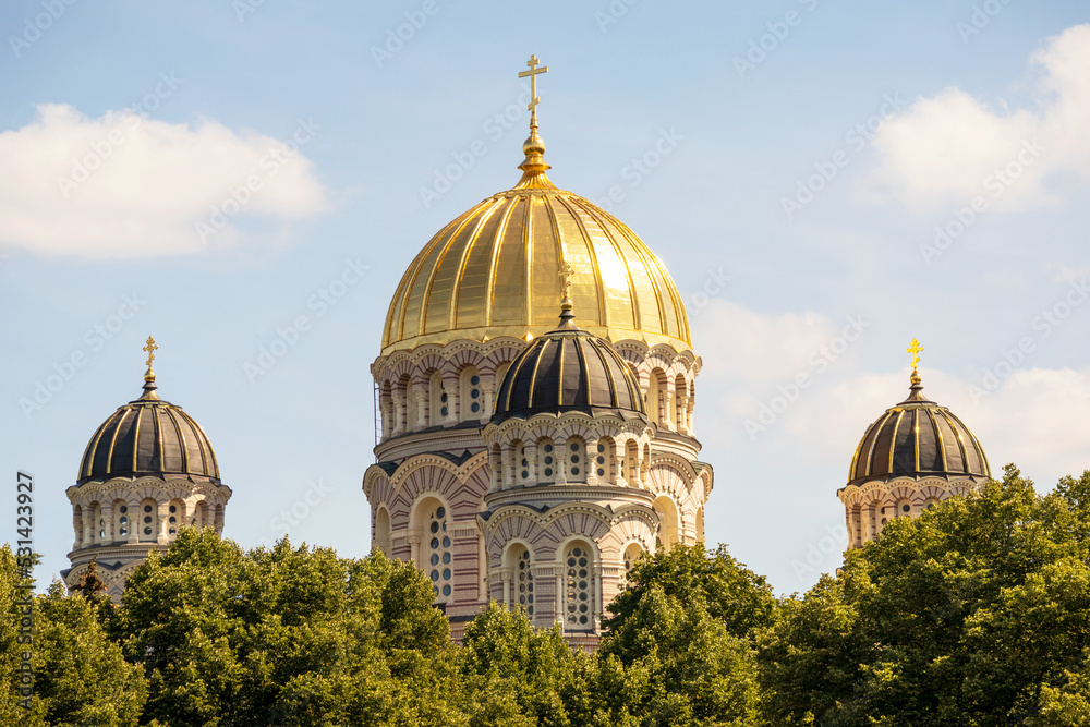 Fototapeta premium A church with a yellow wall and a pointed golden tip in the middle of the city center with multiple windows and trees next to it