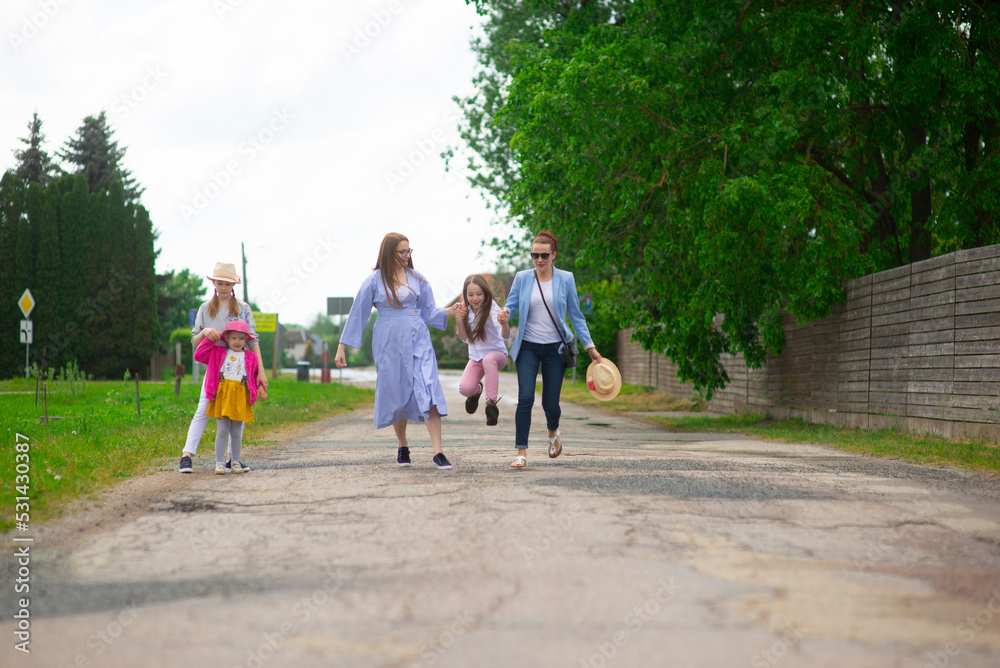 Obraz premium Group of happy family people-two sisters and little girls walking down the city street on a sunny summer day