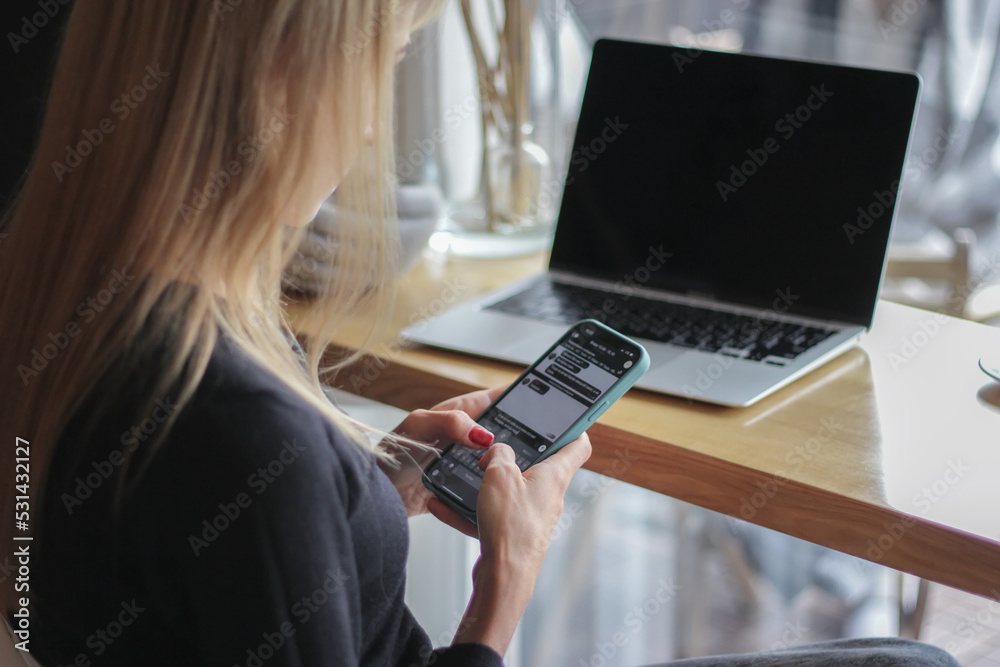 Side image of beautiful woman in striped shirt calling by smartphone while touching a white blank screen computer tablet with keyboard case and sitting at the wooden table with windows as background. Side image of beautiful woman in striped shirt calling by smartphone while touching a white blank screen computer tablet with keyboard case and sitting at the wooden table with windows as background.