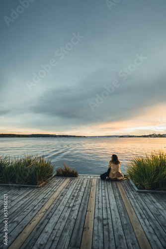 junge Frau sitzt auf einem Steg und blickt auf das Meer am abend in oslo