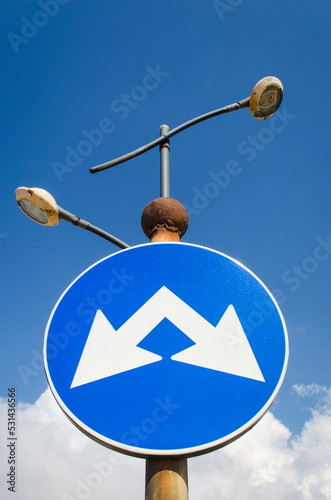 Il segnale blu di un’incrocio a doppia direzione con le frecce bianche che puntano in direzioni diverse photo