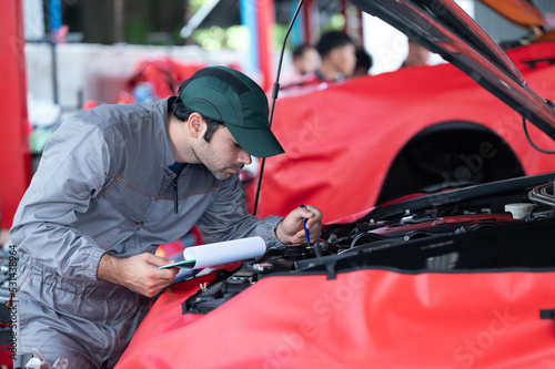 car service, repair, maintenance concept - Arab auto mechanic man or Smith writing to the clipboard at workshop warehouse, technician doing the checklist for repair machine a car in the garage