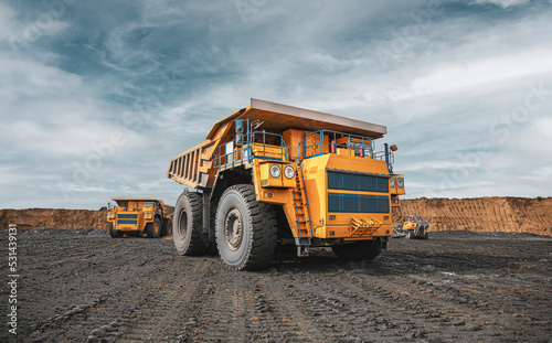 Large quarry dump truck. Big yellow mining truck at work site. Loading coal into body truck. Production useful minerals. Mining truck mining machinery to transport coal from open-pit production