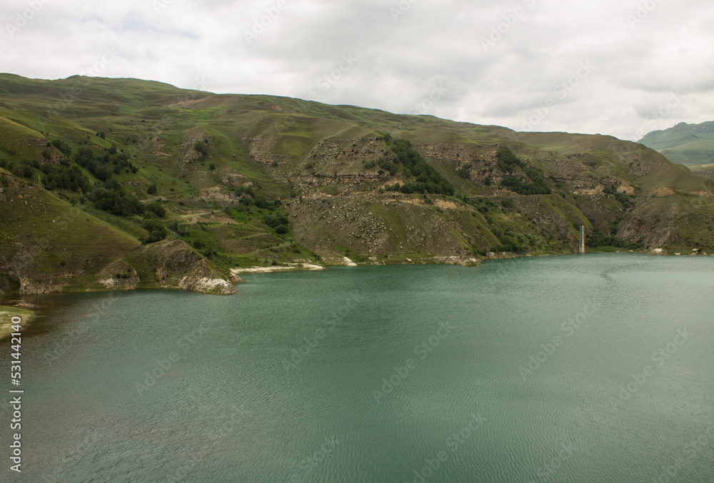 Obraz premium Mountain lake Gizhgit with beautiful turquoise water and high hilly shores on a cloudy summer day and a space for copying in the Elbrus region in the North Caucasus