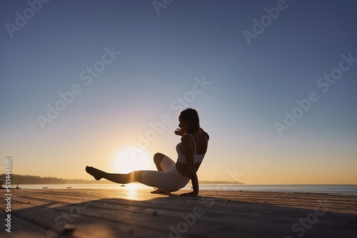 Silhouette young woman practicing yoga on the beach. Caucasian girl exercising yoga in nature  morning at seashore