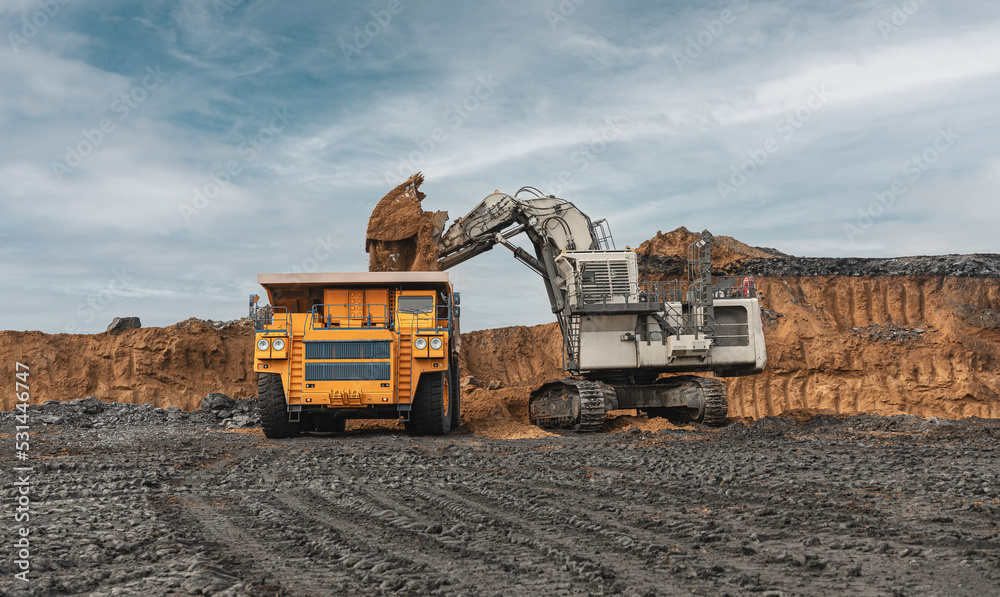 Large quarry dump truck and excavator. Big mining truck work coal deposit. Loading coal into body truck. Production useful minerals. Mining mining machinery to transport coal from open-pit production