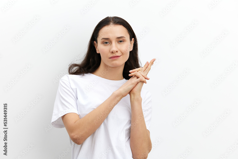 funny, attractive, playful woman shows a pistol sign with her fingers while standing in a white T-shirt on a white background and looking at the camera funny, attractive, playful woman shows a pistol sign with her fingers while standing in a white T-shirt on a white background and looking at the camera