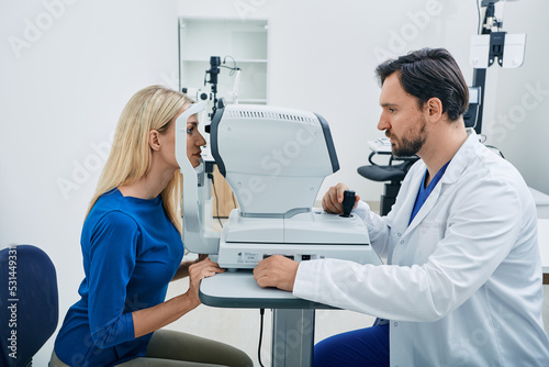 Experienced ophthalmologist man using automated refractor for vision correction female patient in ophthalmic office