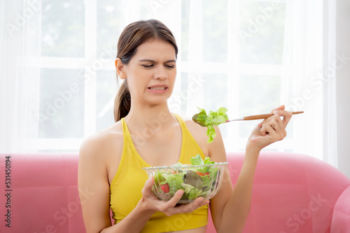 Young caucasian woman sitting on sofa eating vegetable salad while feeling dislike and expression disgusted, woman emotion frustrated with anorexia vegetarian and hate, nutrition food concept.