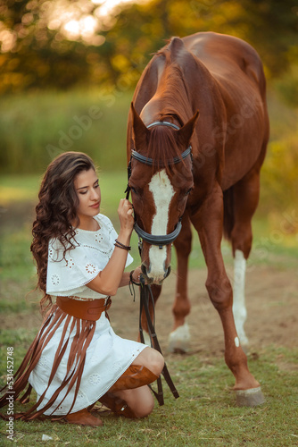 portrait of a young beautiful woman with curly hair who is holding a brown horse. Walking with the animals on the farm. Horse riding. boho style rider