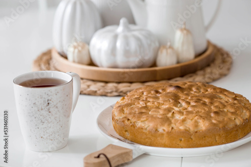 Still-life. Dried pampas grass in a vase, white ceramic pumpkins, candles and apple pie charlotte on a white table in the interior of a Scandinavian-style home kitchen. Cozy autumn concept.