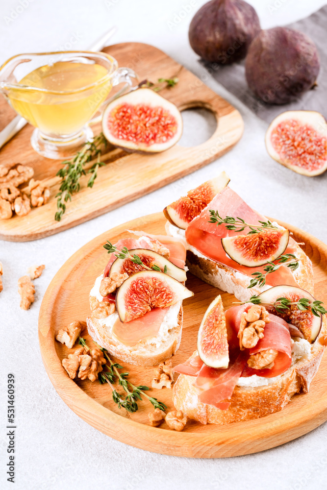Bruschettas with fig, cream cheese, prosciutto, walnuts and honey on wooden plate. Healthy quick breakfast recipe. Vertical image. Selective focus